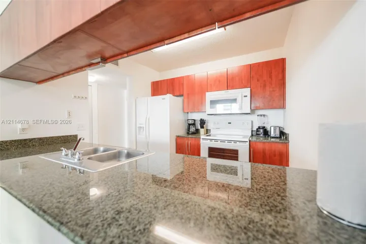 Kitchen featuring wood cabinetry, stone countertops, a dual-basin sink with a chrome faucet, and white appliances