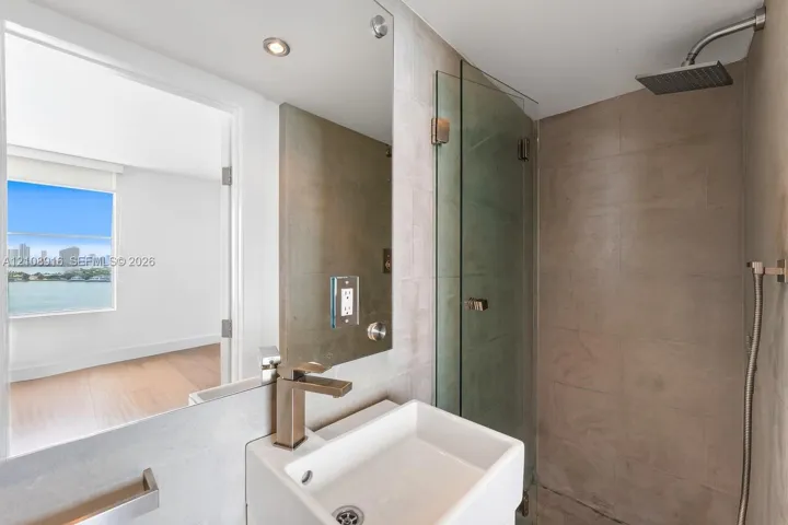 Private bathroom connected to secondary bedroom featuring rainfall shower head as well as convenient handheld shower and natural limestone finishes