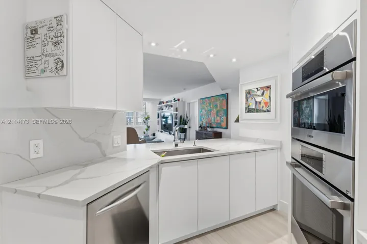Kitchen featuring white cabinetry, veined solid-surface countertops, stainless steel undermount sink, and integrated stainless steel double wall ovens