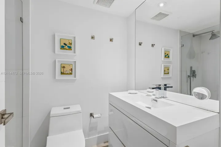 Modern floating vanity with a seamless integrated sink, polished chrome widespread faucet, large-format mirror, and glass-enclosed shower featuring a wall-mounted rainfall showerhead