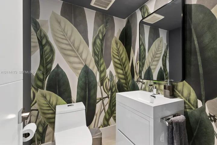 Botanical print wallcovering, white vanity cabinet with a rectangular basin, polished chrome faucet, and black-framed rectangular wall mirror