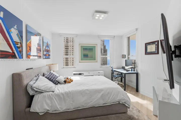 Bright room featuring wood-finish flooring, white walls, triple window configuration, and a square modern flush-mount ceiling light fixture