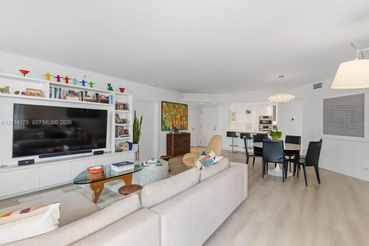 Open-concept floor plan featuring light wood-finish flooring, custom built-in cabinetry with integrated shelving, recessed lighting, and a kitchen island with stone countertop