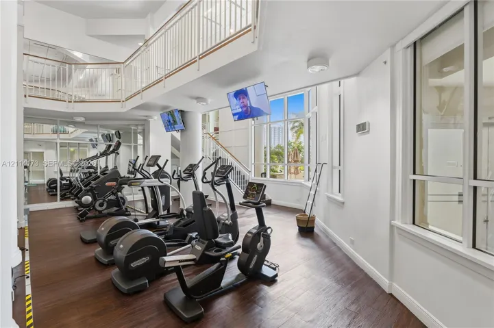 Two-story fitness space featuring wood-finish flooring, floor-to-ceiling windows, an elevated mezzanine railing, and expansive mirrors