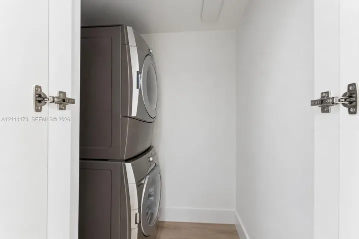 Laundry closet featuring stacked metallic-finish appliances and white cabinetry doors with chrome-finish concealed hinges