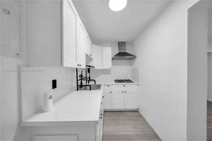 Kitchen featuring white cabinetry, solid-surface countertops, wood-finish flooring, a stainless steel range hood, and a gas cooktop