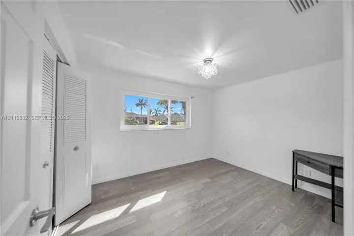 Wood-finish flooring, white louvered closet doors, multi-pane horizontal window, and decorative crystal-style ceiling fixture