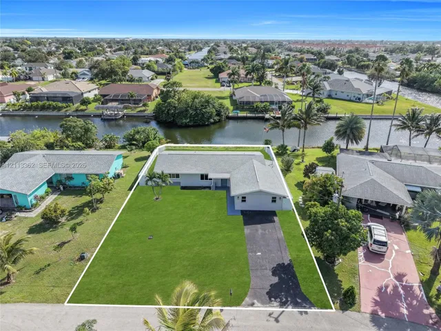 Single-story residence featuring a shingled roof, asphalt driveway, manicured lawn, and waterfront access
