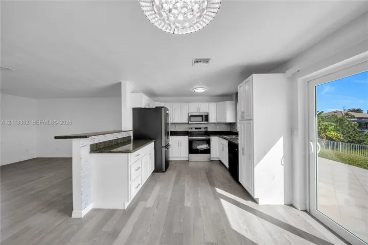 Kitchen featuring white cabinetry, dark stone-finish countertops, stainless steel appliances, wood-finish flooring, and glass sliding doors