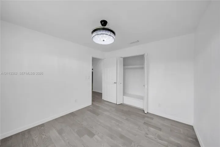 Wood-finish flooring, crystal-accented flush mount ceiling light fixture, and closet with built-in shelving