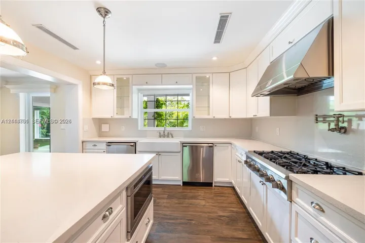 Kitchen featuring white cabinetry, quartz countertops, a farmhouse-style apron sink, professional-grade stainless steel range with matching hood, and wood-finish flooring