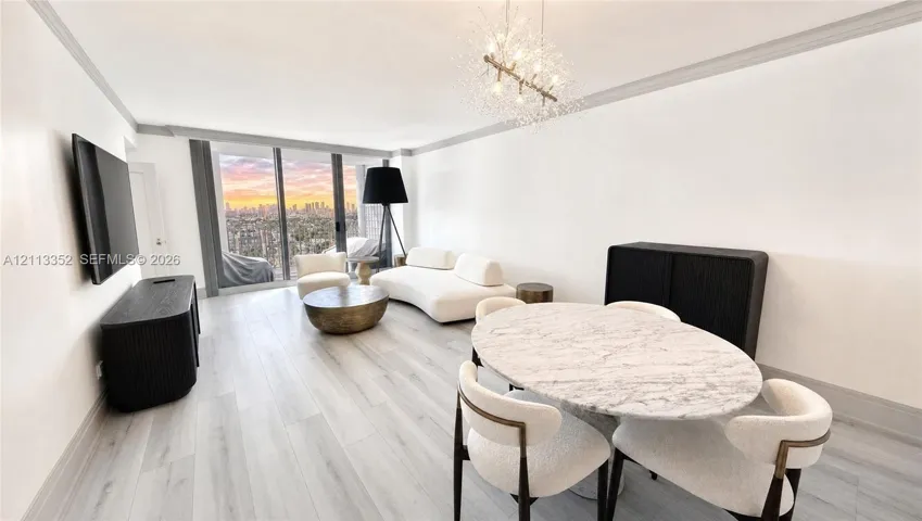 Open-concept living space featuring wood-finish flooring, floor-to-ceiling windows, a metallic starburst chandelier, crown molding, and an expansive cityscape backdrop