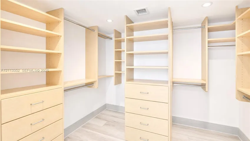 Custom walk-in closet featuring extensive light-finish wood cabinetry, integrated drawer banks, multiple tiered open shelving units, and metal hanging rods