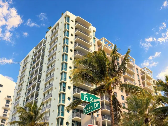 High-rise exterior featuring a light-toned facade, multiple balconies with metal railings, decorative circular windows, and integrated mature palm trees