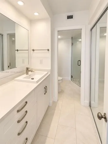 Bathroom vanity featuring white cabinetry, a rectangular vessel sink, and light-toned solid surface countertop, complemented by floor-to-ceiling mirrored closet doors