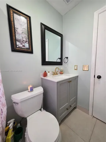 Grey shaker-style vanity with a stone countertop, integrated undermount sink, brushed gold faucet, and a black-framed mirror