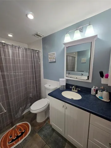 Bathroom vanity featuring a solid-surface countertop, integrated basin, white cabinetry, and three-light vanity fixture above a medicine cabinet
