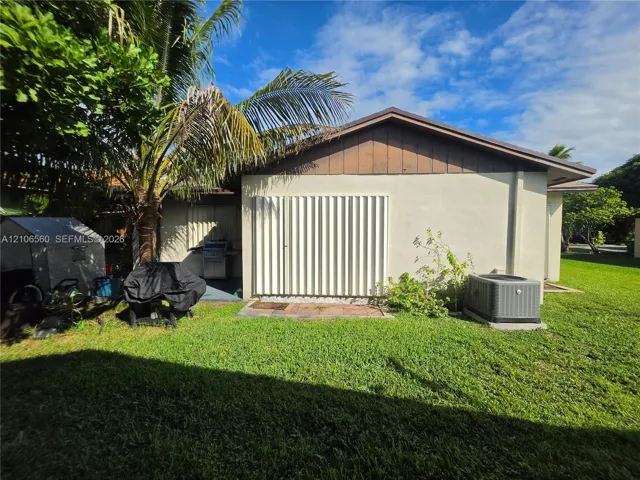 Exterior side profile featuring light-toned stucco walls, vertical wood siding, integrated accordion-style shutters, and a rear lawn