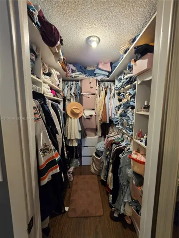 Walk-in closet featuring white built-in shelving, integrated hanging rods, and wood-finish flooring