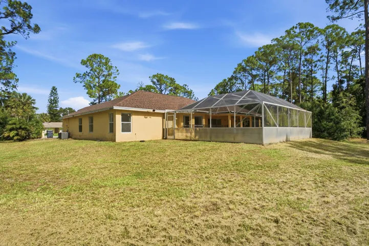 Rear exterior featuring a stuccowork facade, shingled hip roof, and a screened-in lanai enclosure set against a mature tree line