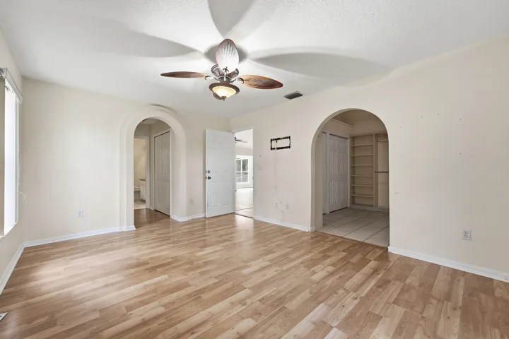 Interior space featuring wood-finish flooring, two arched entryways, ceiling fan with integrated lighting, and built-in shelving