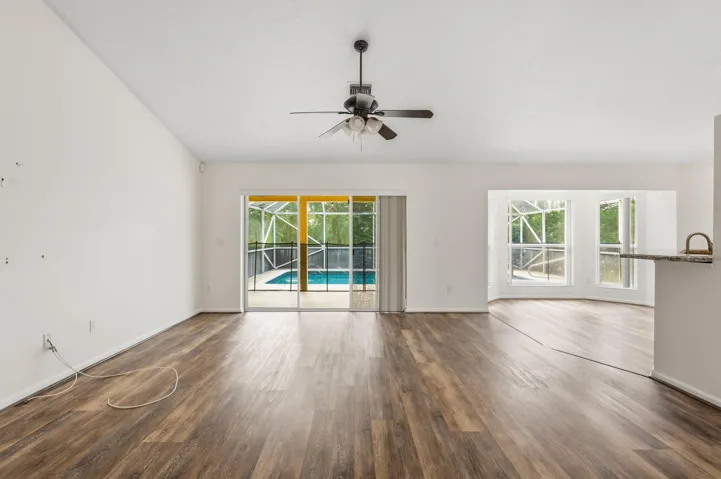 Open-concept interior featuring vaulted ceilings, wood-finish flooring, a ceiling fan, and sliding glass doors revealing a screened-in pool