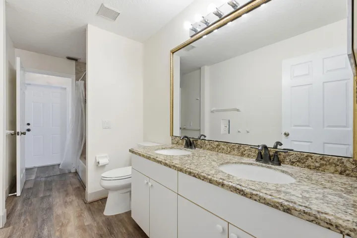 Dual-sink vanity with stone-finish countertop, undermount sinks, bronze-tone fixtures, wood-finish flooring, and large wall-mounted mirror