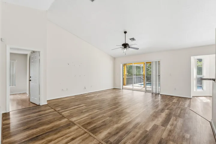 Vaulted ceilings, wood-finish flooring, central ceiling fan, and sliding glass doors providing outdoor access