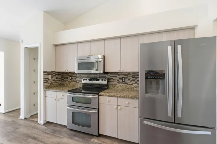 Kitchen featuring light-finish cabinetry, stone-texture countertops, multi-tonal backsplash tile, and stainless steel appliances including a double-oven range and French-door refrigerator