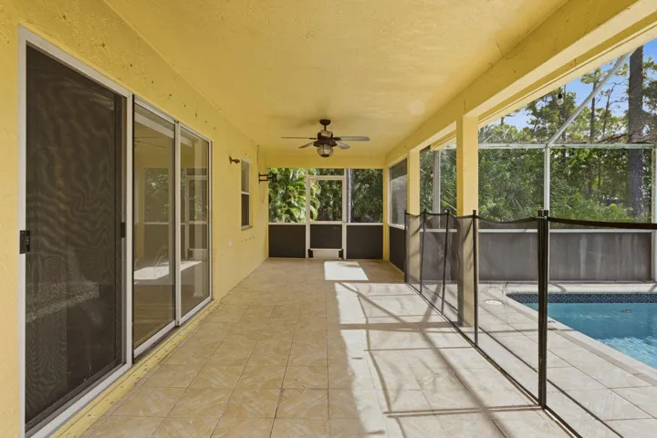 Covered lanai featuring tile flooring, ceiling-mounted fan, screened enclosure, and in-ground swimming pool