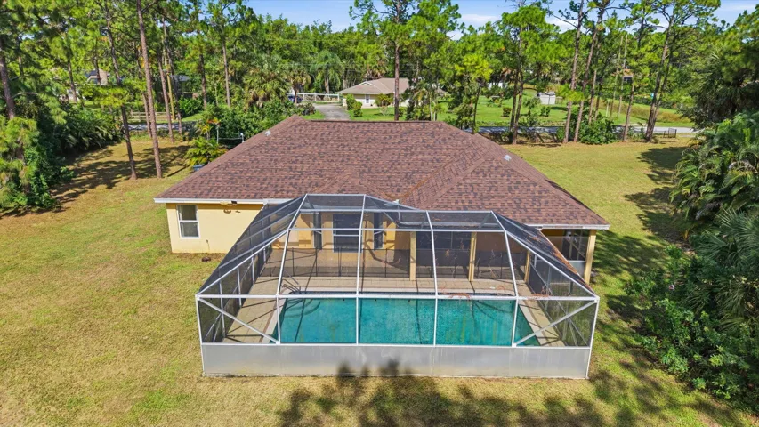 Aerial perspective of a detached residence featuring a screened-in swimming pool, a concrete pool deck, and a multi-sloped roofline situated on a lot with mature perimeter trees