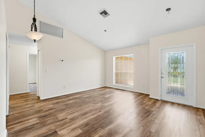 Vaulted ceilings, wood-finish flooring, an exterior door with decorative glass inlay, and a multi-tiered pendant light fixture
