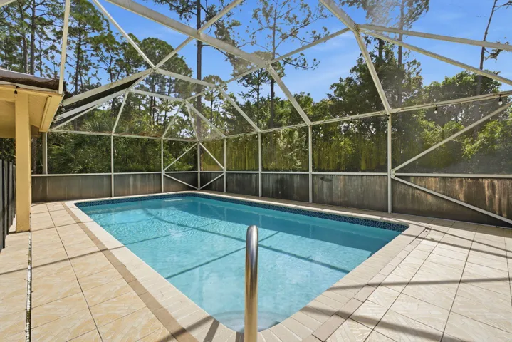 Rectangular swimming pool enclosed by a screened lanai with tile decking and metal perimeter screening