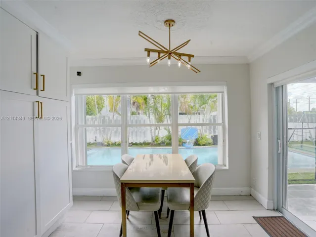 Dining area featuring built-in floor-to-ceiling cabinetry with metallic hardware, large multi-pane windows, gold-tone modern chandelier, and oversized ceramic tile flooring