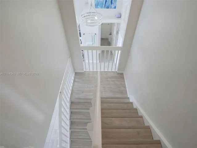 Staircase featuring wood-finish treads, white painted balustrades, and a tiered drum chandelier
