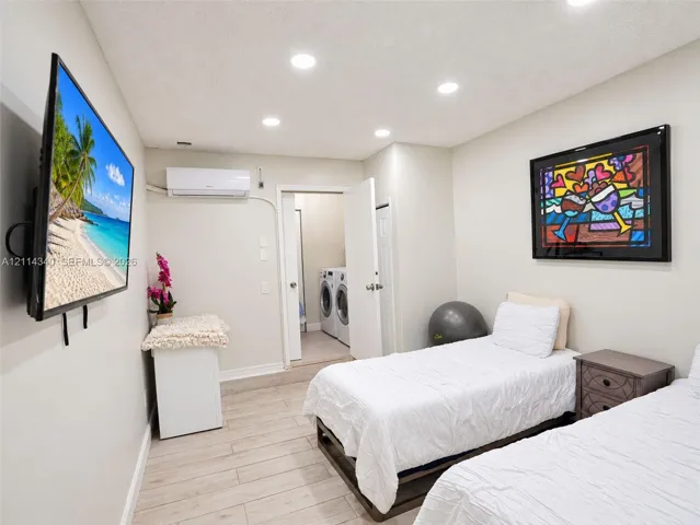 Neutral-toned room featuring recessed ceiling lighting, wall-mounted ductless heating and cooling unit, wood-finish flooring, and a dedicated laundry area