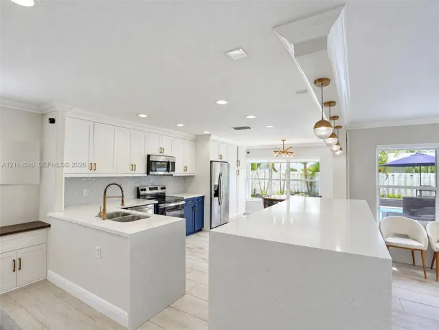 Kitchen featuring an oversized waterfall quartz island, custom white cabinetry with gold-tone hardware, a geometric tile backsplash, stainless steel appliances, and recessed lighting