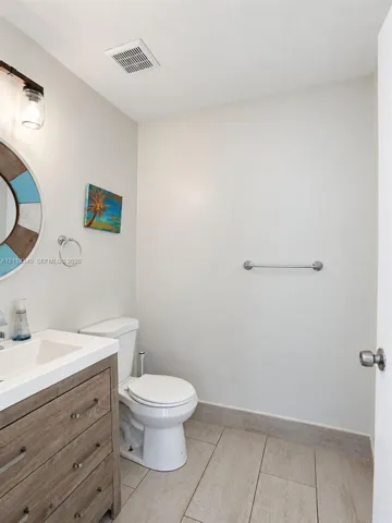Bathroom featuring a wood-finish vanity with an integrated rectangular sink, large-format tile flooring, a wall-mounted metal towel bar, and a multi-light fixture