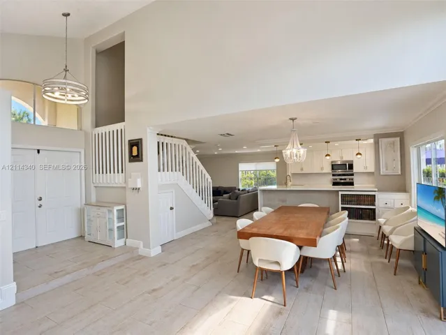 Open-concept interior featuring vaulted ceilings, wood-finish flooring, a tiered staircase with white balusters, and a kitchen equipped with white cabinetry and a built-in oven