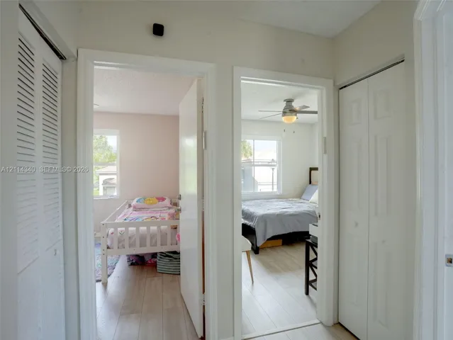 Hallway featuring two sets of white louvered-style bi-fold closet doors, wood-finish flooring, and two interior doorways with light-colored solid-core doors