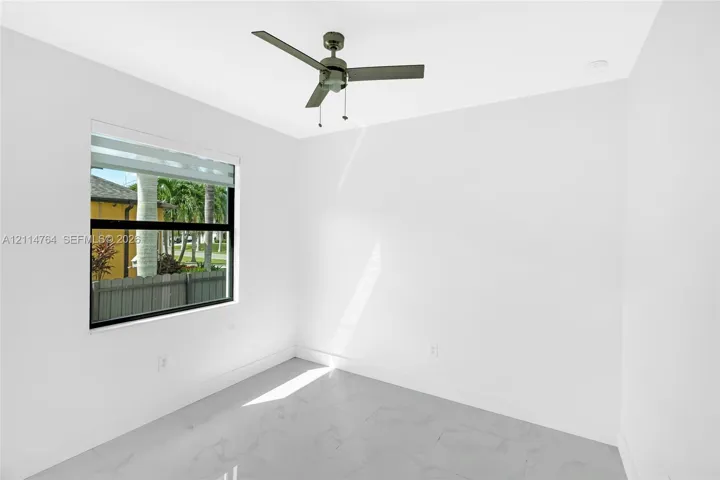 Interior space featuring large-format tile flooring, bright white wall finishes, a multi-blade ceiling fan, and a window with a black frame