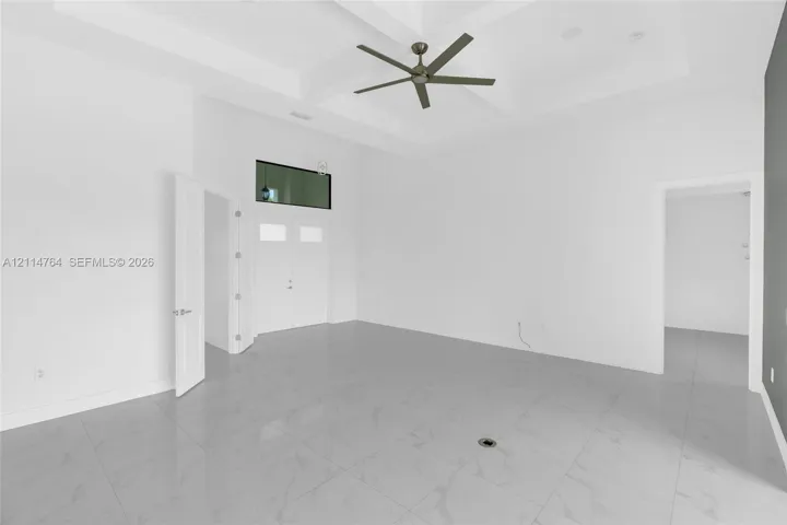 Tray ceiling with a multi-blade ceiling fan, large-format tile flooring, transom window, and solid-core interior doors
