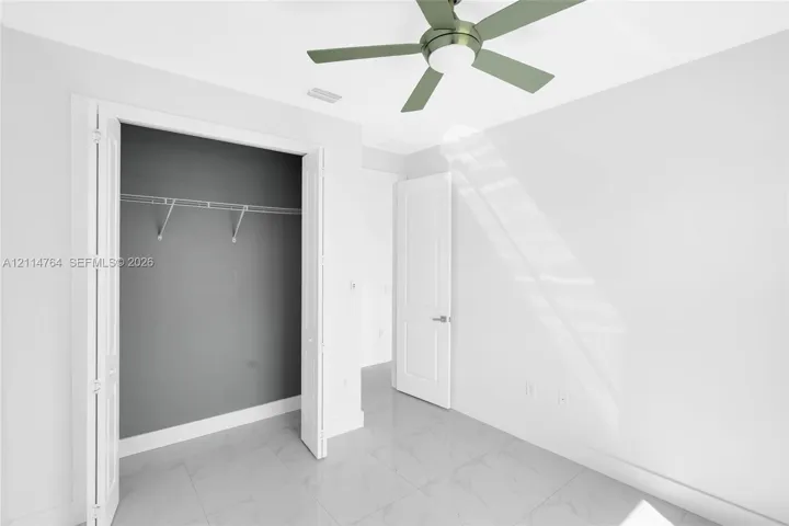 Neutral-toned ceramic tile flooring, ceiling fan with integrated lighting, reach-in closet featuring wire shelving, and two-panel interior door