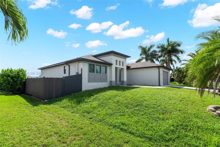 Single-story residence featuring a smooth stucco exterior, attached garage, vertical window detailing, and a private fenced yard with established palm trees