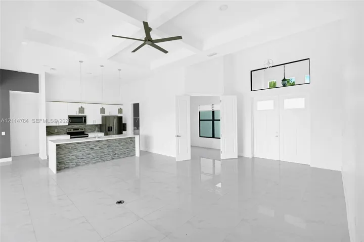 Coffered ceiling with a central fan, large-format tile flooring, kitchen island with stone-finish facade, quartz-style countertops, and double entry doors with a transom window
