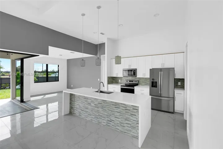 Kitchen featuring white cabinetry, an expansive island with a stone-finish waterfall edge, tile backsplash, stainless steel appliances, and large-format tile flooring