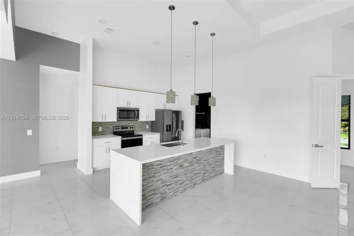 Kitchen featuring white shaker-style cabinetry, quartz countertops, a central island with a decorative stone-tile base, stainless steel appliances, and three glass pendant light fixtures over the island
