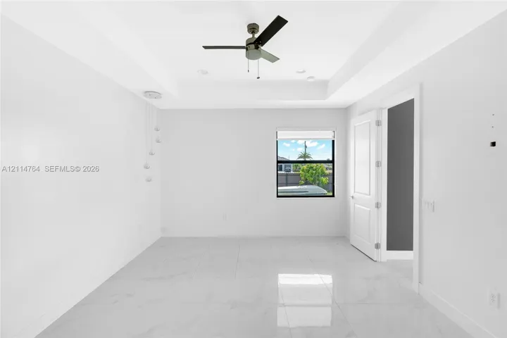 Tray ceiling with a matte black three-blade ceiling fan, large-format tile flooring, and integrated pendant lighting