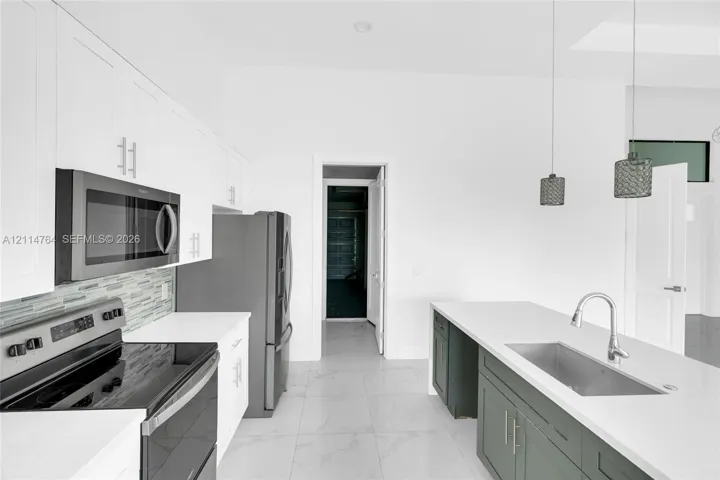 Kitchen featuring white cabinetry, solid-surface countertops, stainless steel appliances, multi-toned tile backsplash, and a central island with an undermount sink
