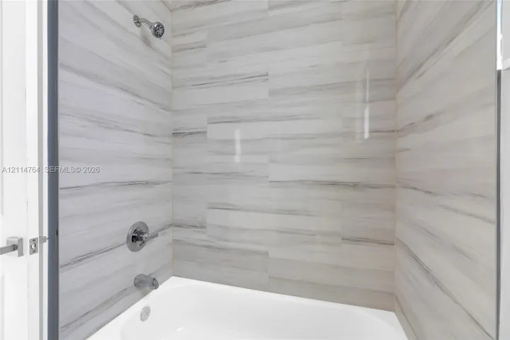 Bathtub alcove featuring horizontal stone-patterned wall tile, chrome shower head, chrome faucet, and integrated diverter